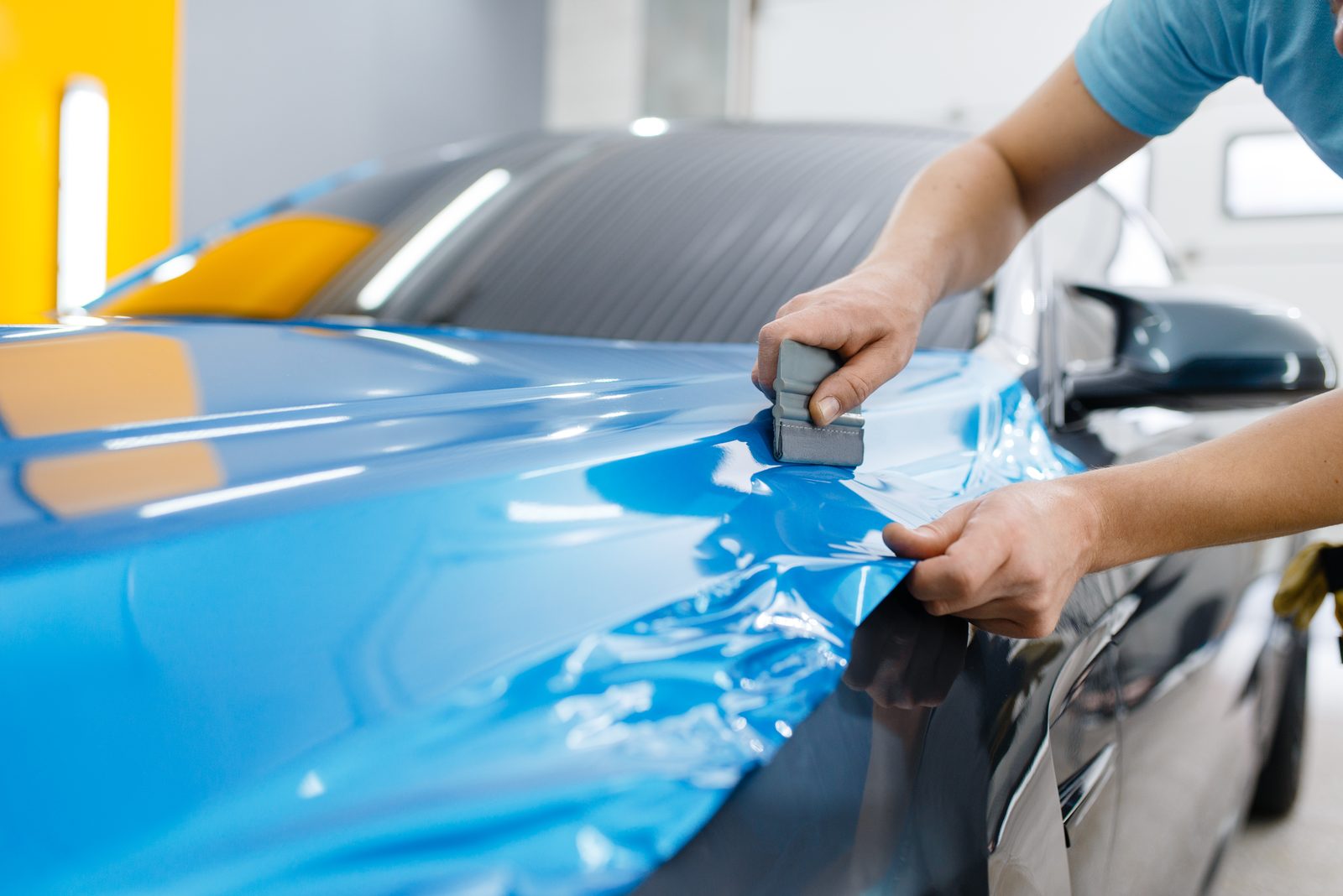 Auto wrappen Lelystad - blauwe wrapfolie aanbrengen Specialist brengt blauwe wrapfolie aan op de motorkap van een auto tijdens auto wrappen in Lelystad