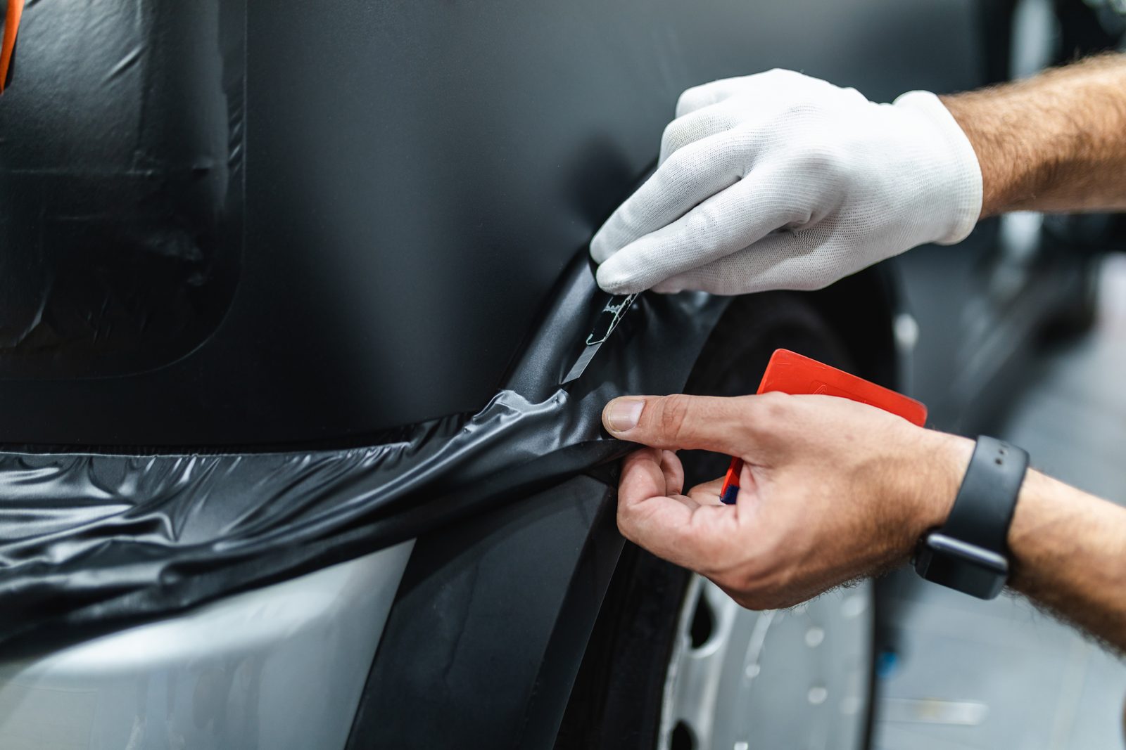 Monteur brengt met een rakel zwarte folie strak aan op een auto bij een foliespecialist in Lelystad
